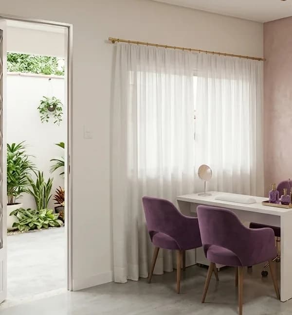Ambiente do Studio Carla Paes: mesa de atendimento branca com poltronas de veludo roxo, cortina clara e parede rosé
